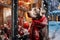 A Weimaraner dog wearing a red Christmas scarf against the backdrop of a city street, next to a Christmas store window