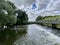 Weir over River Great Ouse, Wyton, England. Blue cloudy sky with trees and footbridge.