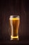 Weizen beer glass with golden sparkling lager on dark wood board.