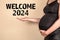 Welcome 2024 Concept. A pregnant woman points to the text