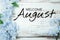 Welcome August text and blue flower decoration on wooden background