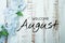 Welcome August text and blue flower decoration on wooden background