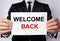 Welcome back inscription on a white sheet of paper in the hands of a businessman on a white background. The concept of returning