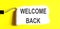 WELCOME BACK One open can of paint with white brush on it on yellow background. Top view