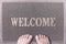 Welcome Door Mat With Female Feet. Friendly Grey Door Mat Closeup with Bare Woman Feet Standing. Welcome Carpet.