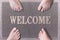 Welcome Door Mat With Funny Family Feet. Friendly Grey Door Mat Closeup with Four Bare Feet Standing. Four Feet on