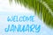 Welcome January text on the background with palm leaf and blue sea. Template of a greeting card, postcard or