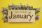 Welcome January text on wooden board with flowers frame on yellow background