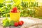 Welcome July text and red strawberry berries in yellow mug on stump in garden, summer sunny day. Front view