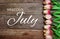 Welcome July text and tulip flower decoration on wooden background