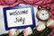 Welcome July written on blue frame with tulip flower flat lay on marble background