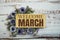 Welcome March text on wooden board with flowers frame on wooden background