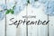 Welcome September text and blue flower decoration on wooden background