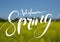 Welcome spring handwriting lettering design on blurry blossom field landscape.