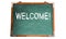 Welcome! text message in white chalk written on a school green old grungy vintage wooden chalkboard or blackboard