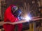 Welder bends to cut metal beam with orange sparks.