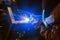 Welder in a protective mask in a dark shop floor weld metal parts. Sparks flyng