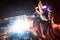 Welder in a protective mask in a dark shop floor weld metal parts. By welding sparks fly in different directions