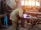 Welder in protective suit at the factory welds parts, workshop, sunset