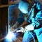 Welder in work clothes working on a workpiece in an industrial company