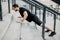 Well built young man pushing up from stairs. Side view. Athletic man with black hair wearing black sportswear and