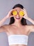 Well then, what do we have here. Studio shot of an attractive young woman holding oranges in front of her eyes against a