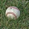 A well-used softball in the grass.