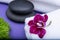 Wellness Relax concept with Spa elements. Rolled up White Towels, Orchid, stacked Basalt Stones, and Dianthus Flowers on purple
