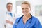 Were dedicated to keeping you healthy. Portrait of a female doctor in scrubs with a colleague standing in a the