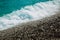 Wet black pebble beach covering with frothy water of waves. Background, texture