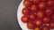 Wet cherry tomatoes on a white plate with a blue border close-up on a gray stone surface