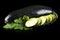 Wet courgettes cut into slices and leaves on black