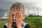 Wet, dirty and sad child covered his face with his hands outdoors on the industrial background with corn field and power station
