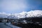 Wet mountain road winding through rough terrain towards snow blanketed mountain range. Dazing snow clouds creeping over