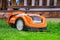 Wet orange automatic lawn robot mower at charging station, close to wooden terrace