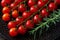 Wet ripe red cherry tomatoes on the vine and sprig of fresh rosemary on a black plate. Macro. Water drops on a small round