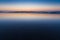 The wet, rippled sand of a beach reflects purple and yellow hues of sunset