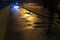 Wet sidewalk with puddles at night. Bicyclists use warning front blue light for safety reason. Selective focus