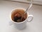 A wet used disposable tea bag lies at the bottom of a dirty ceramic cup in the remnants of unfinished tea