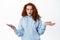 What does it mean. Confused and questioned redhead woman shrugging shoulders while holding mobile phone, staring