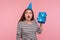 What`s inside? Portrait of girl with party cone hat holding gift box near ear and listening, guessing birthday surprise