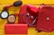 What& x27;s in the women& x27;s bag? A red bag, leather purse, headphones, mirror, comb, perfume bottle on a yellow wooden table.