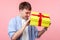 What is there? Portrait of curious happy brown-haired man unpacking present. indoor studio shot isolated on pink background