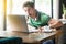 What? Young shocked businessman in green t-shirt sitting, looking and reading some unbelievable news at laptop screen, surprised