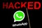 WhatsApp logo on the smartphone screen in a dark room and the word `Hacked` at the blurred background. Selective focus