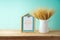 Wheat in vase and photo frame on wooden table over blue wall background. Shavuot holiday mock up for design