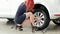 Wheel changing with car spanner, girl sits near car and trying to replace tyres indoor, auto service