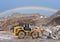 Wheel loader at landfill on rainbow background. Disposal of construction waste and concrete crushing.