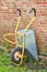 Wheelbarrow against the side of a red brick wall or house. Doing gardening or cleanup work in a backyard garden on a