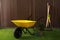 Wheelbarrow, gardening tools and plants on grass near wood slat wall